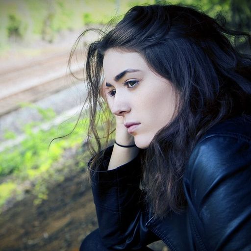 a woman in a black jacket is sitting on the ground with her head resting on her hand .