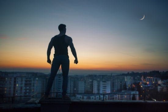 a man is standing on top of a building overlooking a city at sunset .