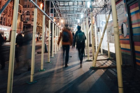 a couple of people are walking down a sidewalk under a scaffolding .