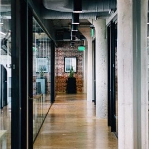 a long hallway in an office building with glass doors and a brick wall .