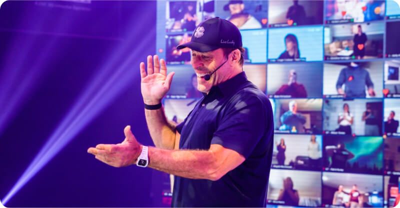 a man wearing a hat and a microphone is standing in front of a large screen .