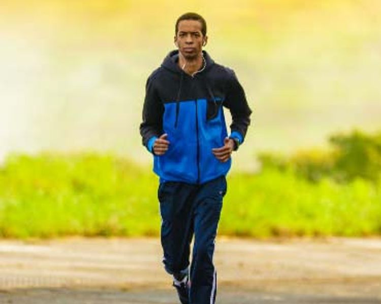 a man in a blue jacket and blue pants is running down a road .