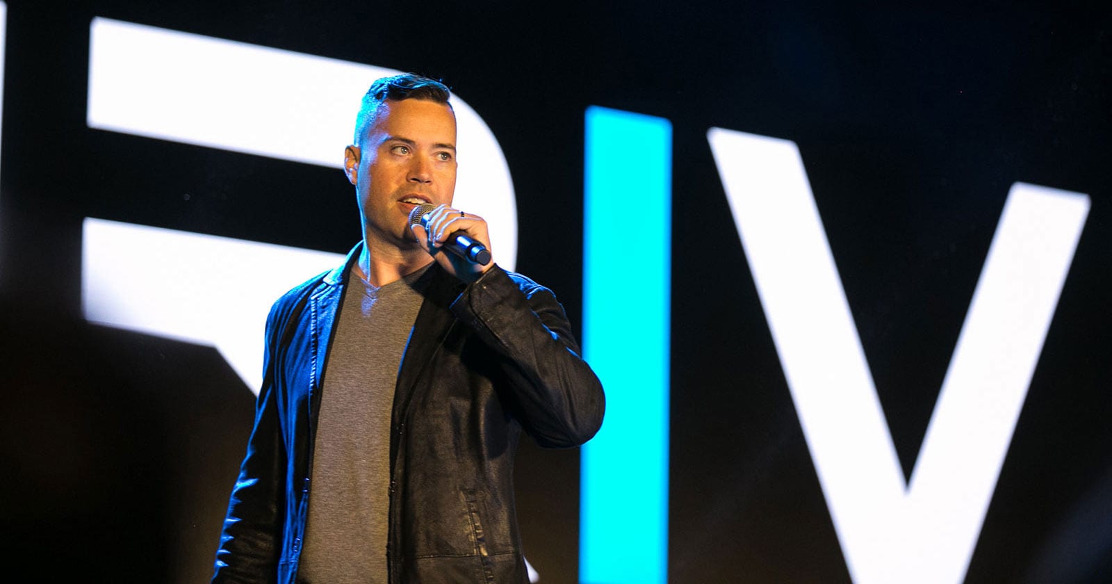 Jordan Harbinger in a leather jacket is standing in front of a microphone