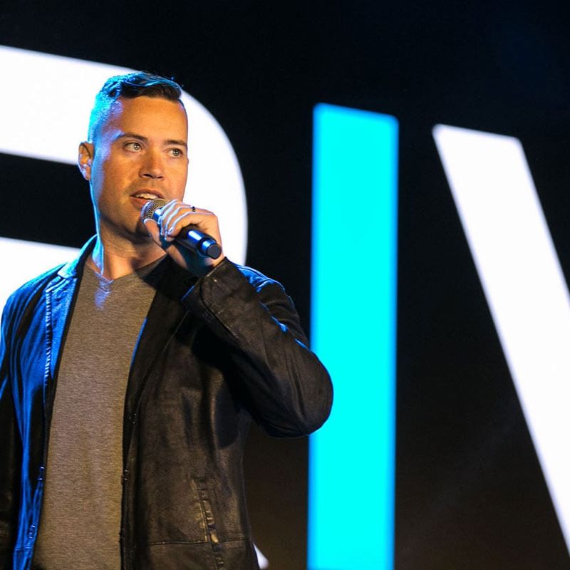 Jordan Harbinger in a leather jacket is standing in front of a microphone