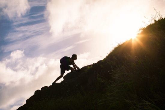 a person is climbing up a hill at sunset .