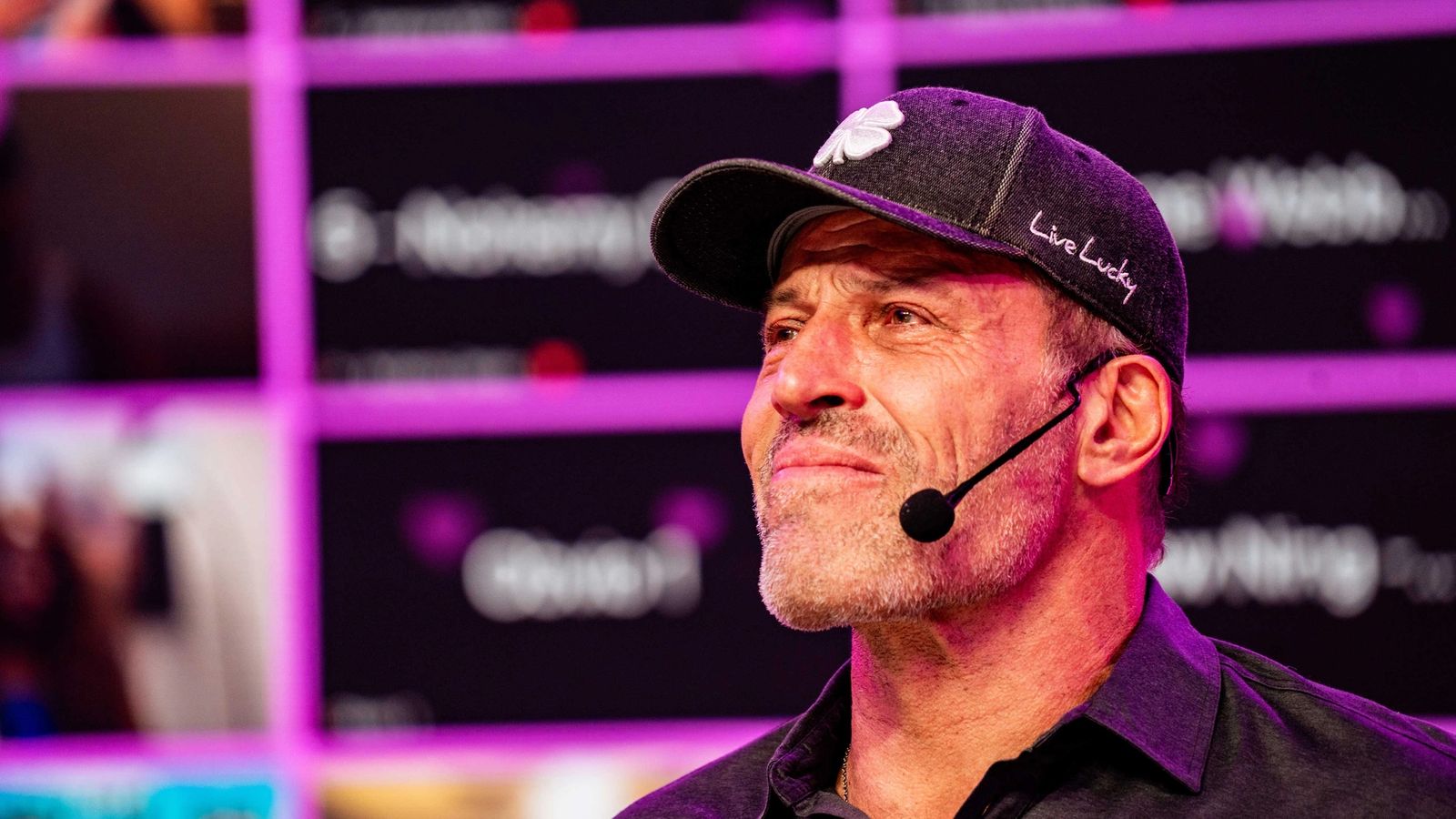 a man wearing a hat and a microphone is standing in front of a purple wall .