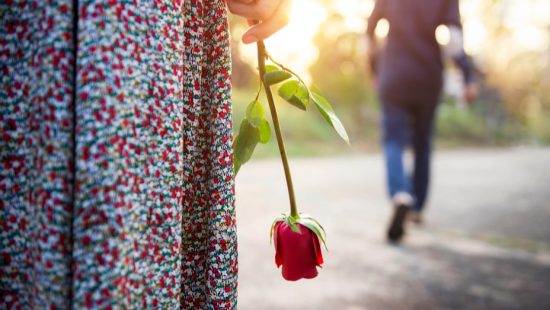 a woman is holding a red rose in her hand and a man is walking in the background .
