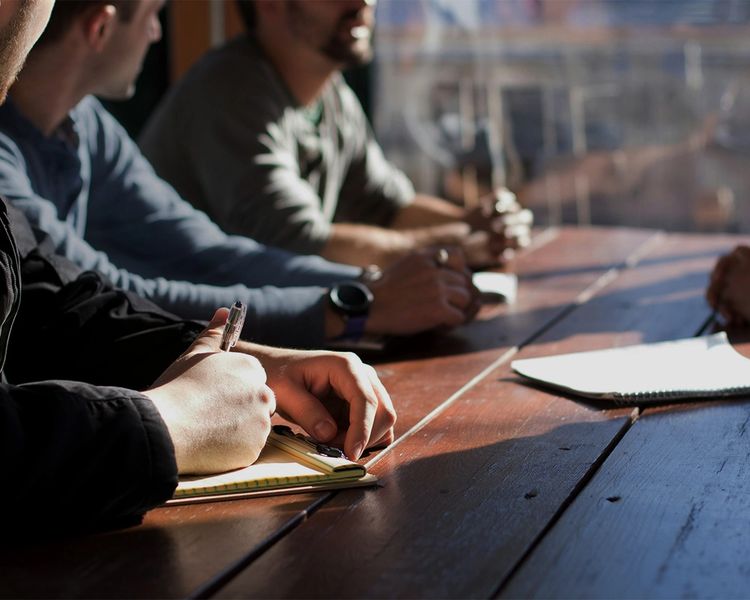 a group of men are sitting around a wooden table having a meeting .