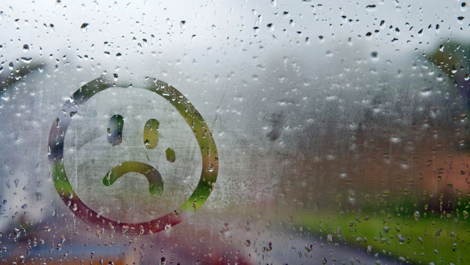 a sad face is drawn on a window with rain drops .