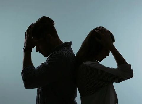Silhouetted man and woman standing back-to-back, hands on heads, looking down in distress.