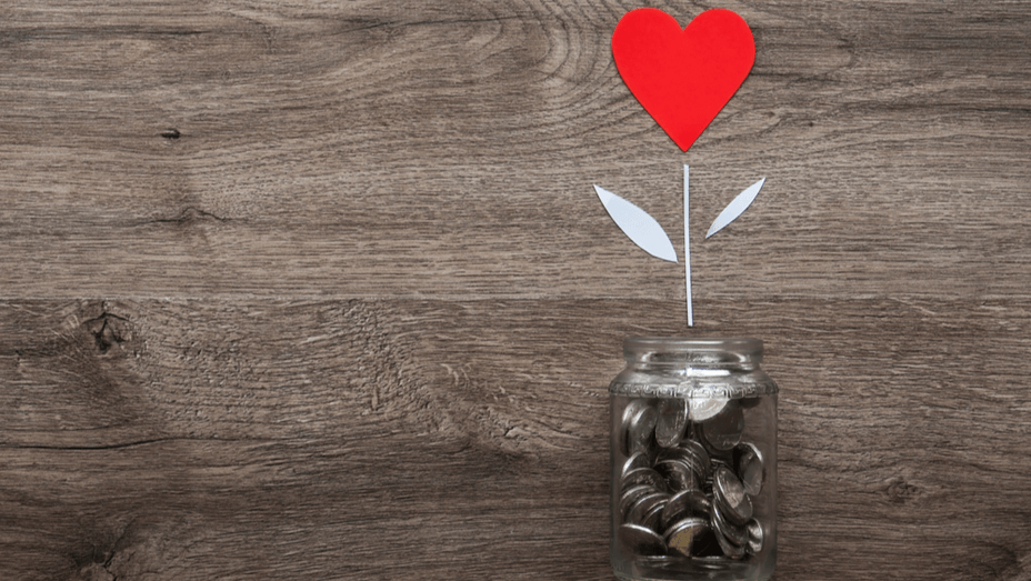 a jar of coins with a paper heart growing out of it