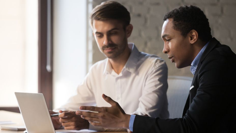 two men are sitting at a table looking at a laptop computer .