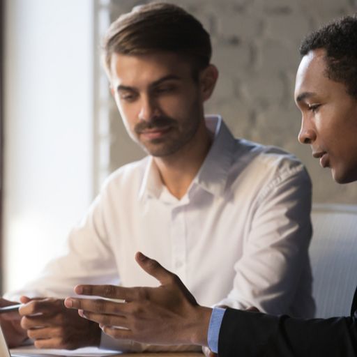 two men are sitting at a table looking at a laptop computer .
