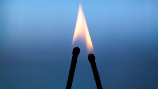 two matches are lit up in the shape of an arrow against a blue sky .