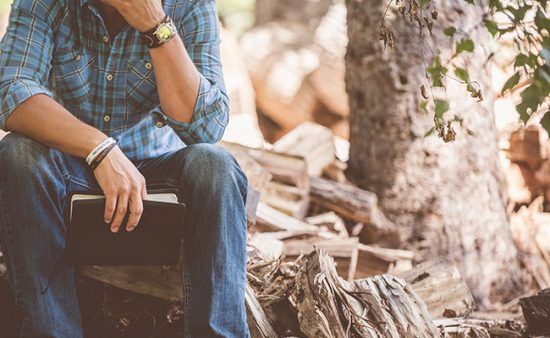 a man is sitting on a log holding a bible .