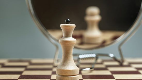a wooden chess piece is standing on a chess board in front of a mirror .