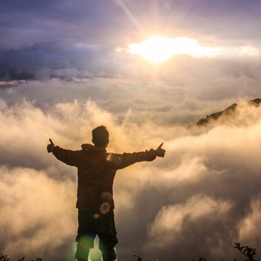 a man is standing on top of a mountain with his arms outstretched .