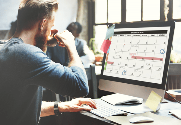 a man drinking coffee while looking at a calendar on a computer