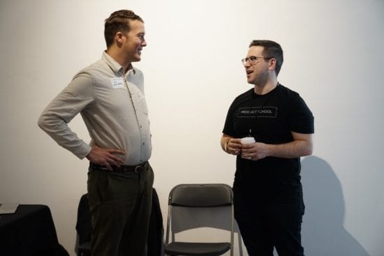 two men are standing next to each other and talking in a room .