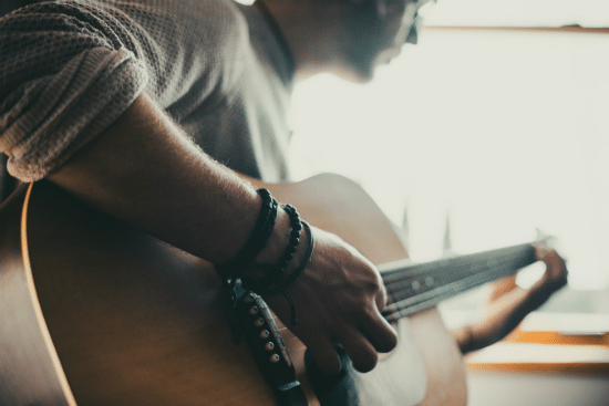 a man wearing bracelets is playing an acoustic guitar