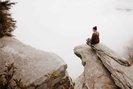 a woman is sitting on the edge of a rocky cliff .
