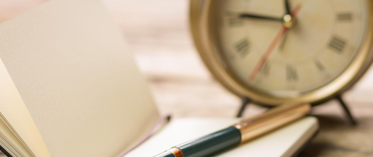 a pen is sitting on top of a notebook next to an alarm clock .