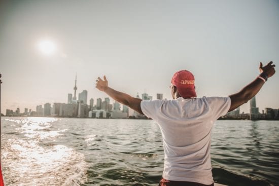 a man is standing on a boat with his arms outstretched in front of a city skyline .