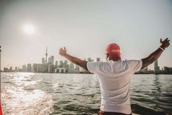 a man is standing on a boat with his arms outstretched in front of a city skyline .