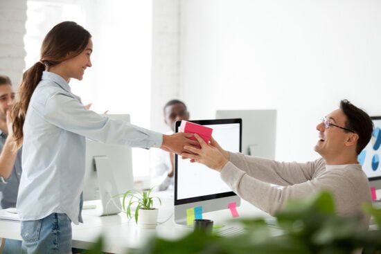 a man is giving a gift to a woman in an office .