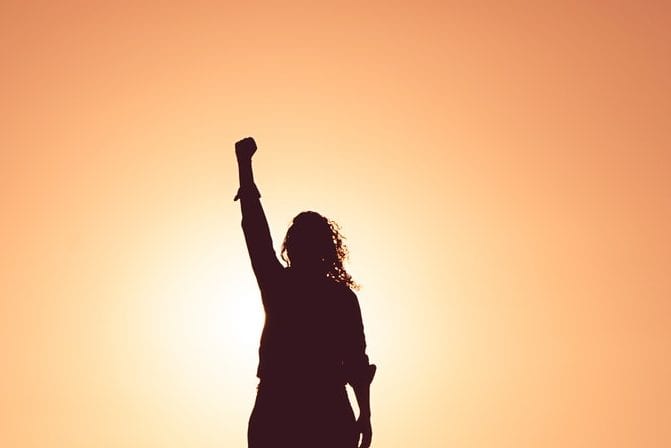 a silhouette of a woman raising her fist in the air at sunset .