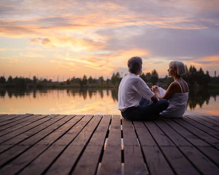 Senior couple holding hands on a dock by a lake at sunset.