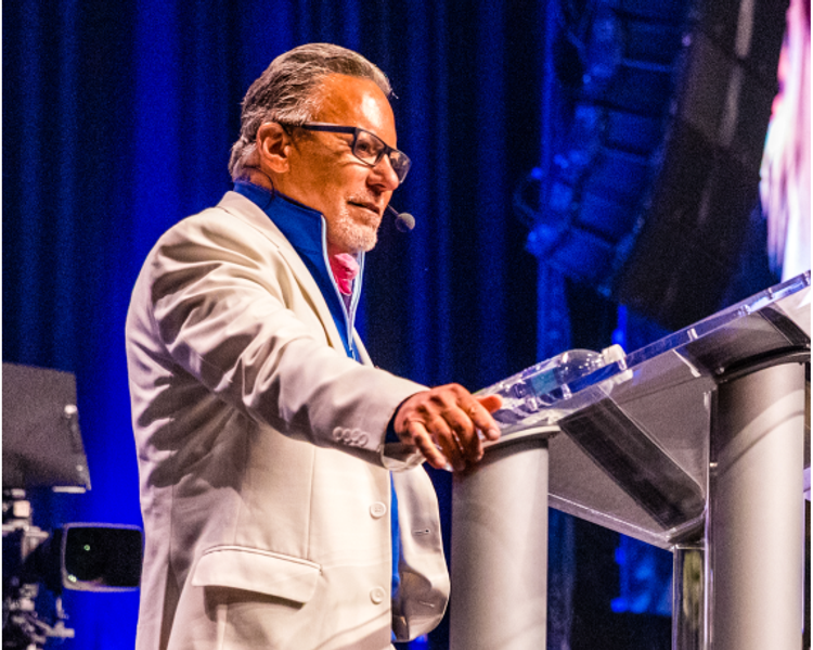 a man in a white suit stands at a podium with a microphone