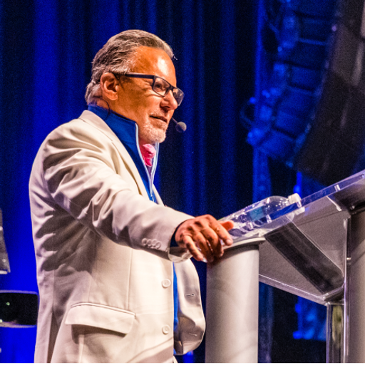 a man in a white suit stands at a podium with a microphone