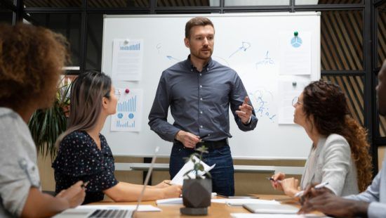 a man is giving a presentation to a group of people sitting around a table .