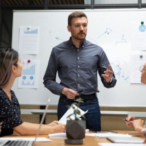 a man is giving a presentation to a group of people sitting around a table .