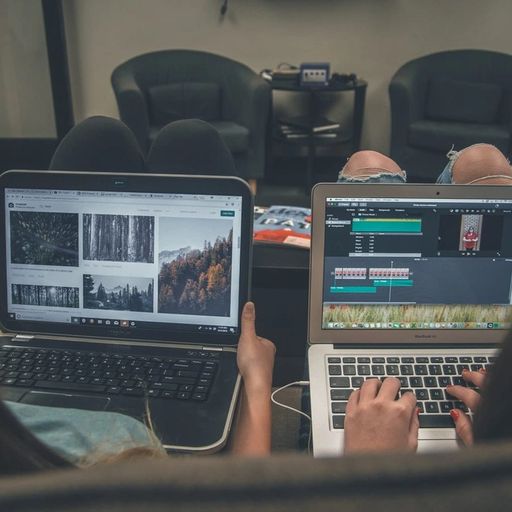 two people are sitting on a couch using laptops .