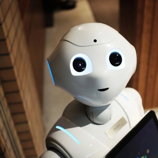 a white robot is holding a tablet and looking at the camera .