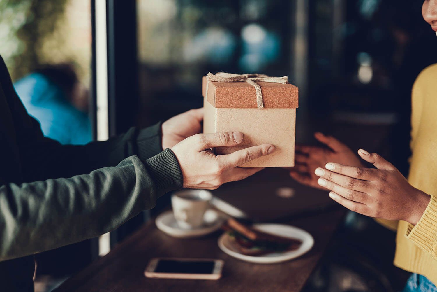 Hands exchanging a brown gift box tied with twine.