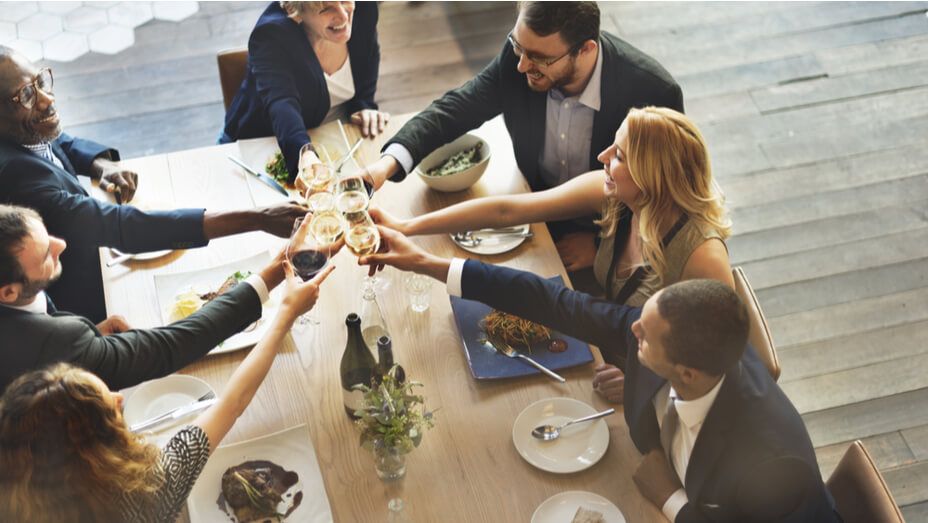 a group of people are sitting around a table toasting with wine glasses .