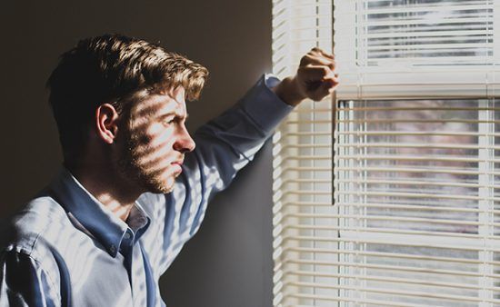a man is looking out of a window with blinds open .