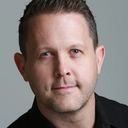 a man is standing in front of a brick wall with his hands in his pockets .