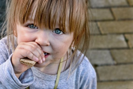 a little girl is eating a cookie with her hand in her mouth .