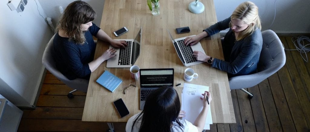 three women are sitting at a table with laptops .