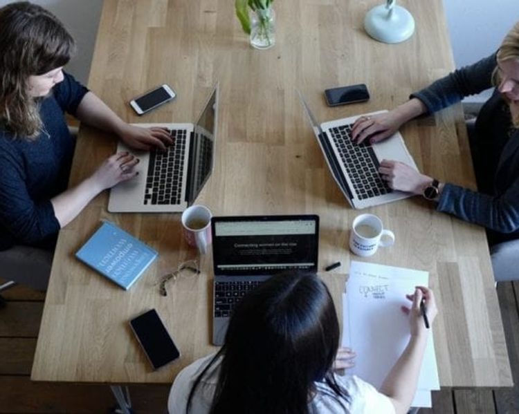three women are sitting at a table with laptops .