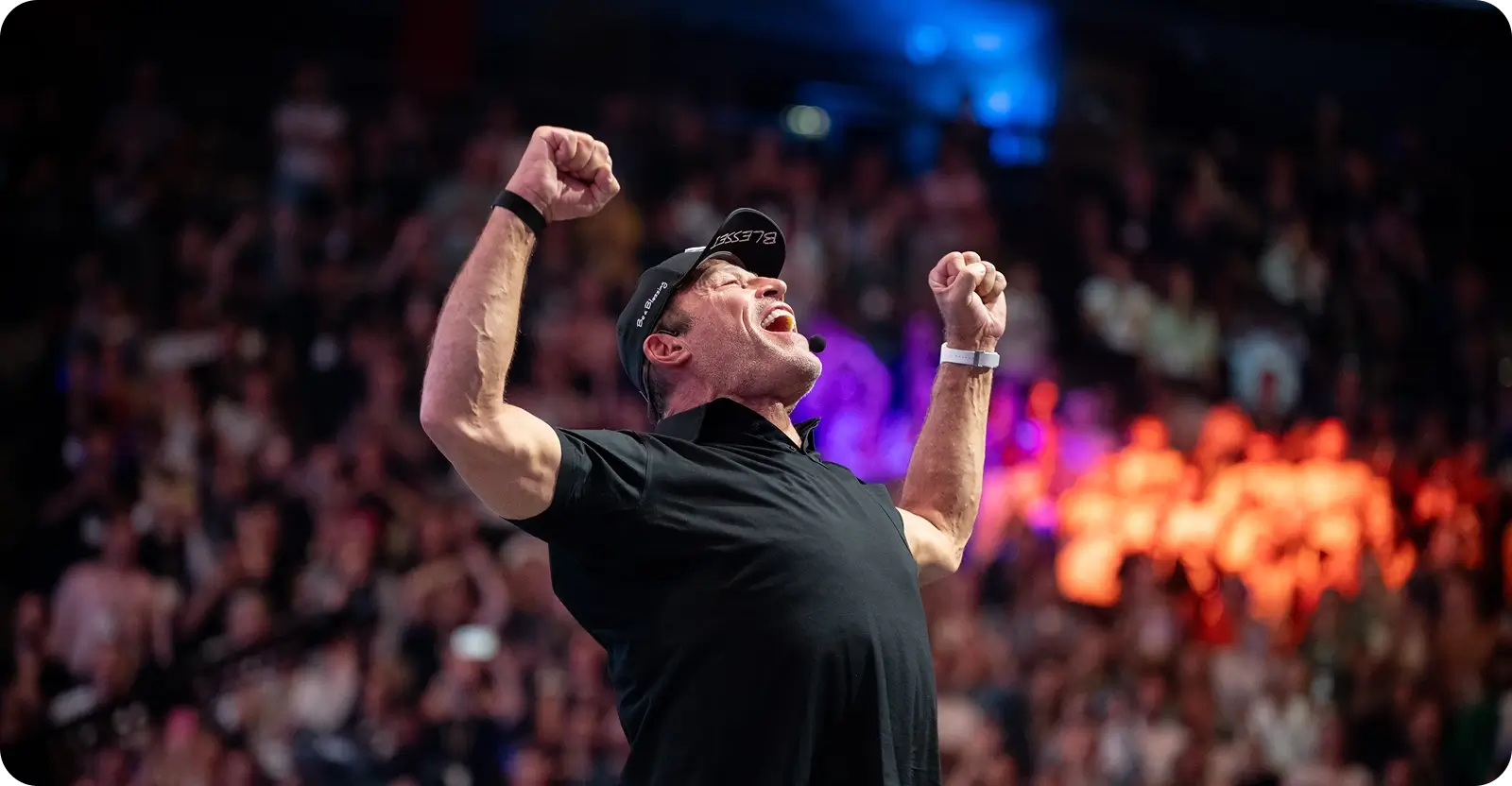 Motivational speaker Tony Robbins with fists raised high, roaring to an arena crowd.