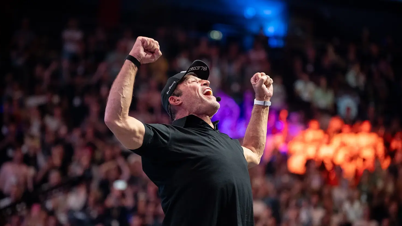 Motivational speaker Tony Robbins with fists raised high, roaring to an arena crowd.