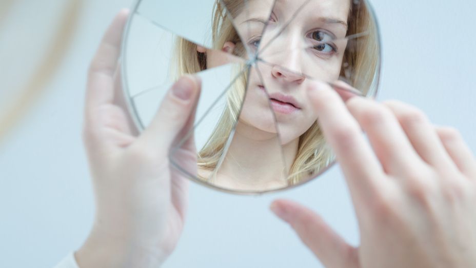 a woman is looking at her reflection in a broken mirror .