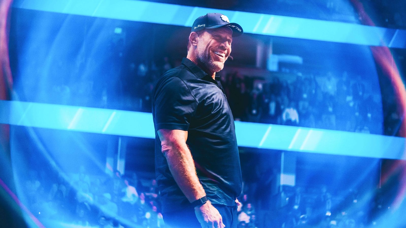 Tony Robbins smiling on stage under vibrant blue lights.