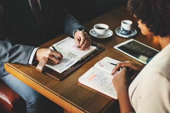 a man and a woman are sitting at a table writing in notebooks .