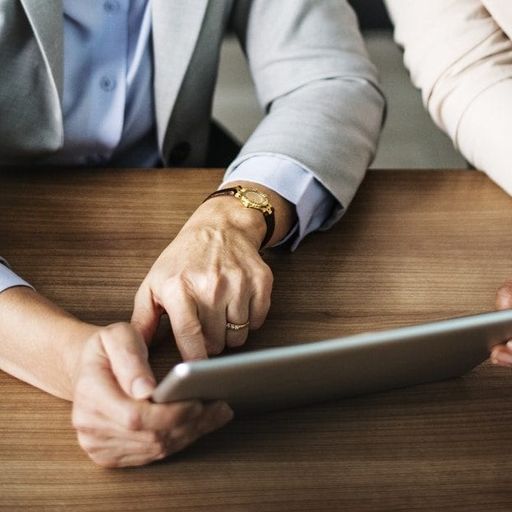 two women are sitting at a table looking at a tablet .